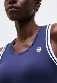 Κοντινό πλάνο ενός ατόμου που φοράει μπλε σκούρο αμάνικο μπλουζάκι K-Swiss με λευκή και μπλε ρίγα στο τελείωμα στους ώμους, εμφανίζοντας το λαιμό και την κλείδα.