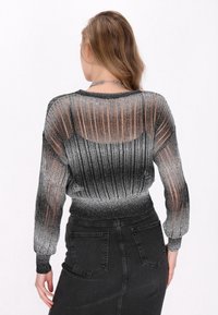 Pulover tricotat argintiu și negru cu dungi transparente, cu mâneci lungi și tiv ajustat, asortat cu o fustă din denim neagră. Contraste subtile de textură vizibile.