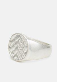 Anel de prata com uma banda arredondada e um topo plano texturizado e padronizado que exibe um design geométrico.