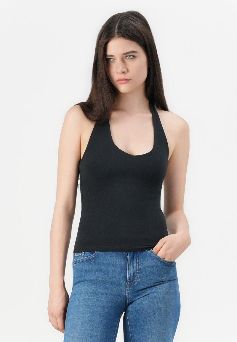 Débardeur noir à col halter avec un design ajusté, texture lisse et décolleté plongeant, associé à un jean en denim bleu.