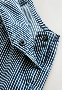 Blau-weißer, senkrecht gestreifter Stoff mit schwarzen Druckknöpfen, auf einer hellen Oberfläche gefaltet.