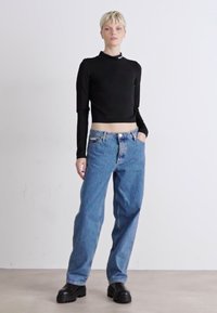 Haut noir coupé à manches longues, jeans en denim bleu à coupe ample, et bottes noires à semelle épaisse. Tissu lisse, design décontracté et coupe relaxée.