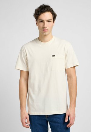 Cremfarbener Baumwoll-T-Shirt mit rundem Ausschnitt, kurzen Ärmeln und einer Vorderasche. Verfügt über ein kleines schwarzes Markenetikett auf der Tasche.