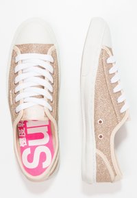 Zapatillas de lona en color rosa dorado brillante con cordones blancos, puntera de goma y plantilla rosa que presenta el texto "SUN". Lateral con un detalle de ventilación adicional.