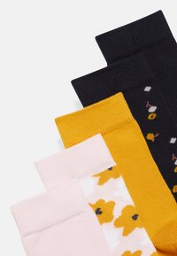 Cinco pares de calcetines: negros, mostaza, rosas con patrón floral y un diseño blanco con flores amarillas. Cada uno presenta un diseño de puño ribeteado.