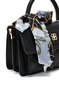 Zwarte leren handtas met een gequilt textuur, gouden hardware en een zijden sjaal om het handvat geknoopt met een zwart en gouden patroon.