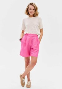 Lichtgewicht crème trui met een gestructureerd patroon en korte mouwen, gecombineerd met felroze hoge taille shorts en beige sneakers.