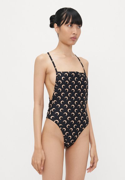 Costum de baie dintr-o singură piesă, cu un fundal negru și un model de lună în formă de semilună în nuanță de piersică. Are bretele subțiri și un design cu decupaj înalt pe picior.