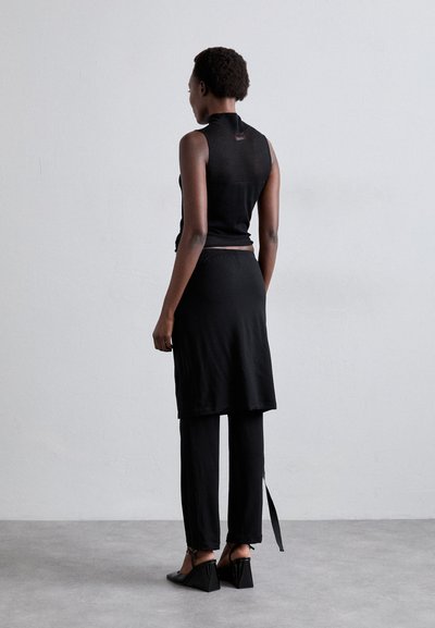 Top preto sem mangas com um colarinho alto, emparelhado com uma saia até ao joelho e calças pretas largas. Os sapatos têm um design de salto alto.