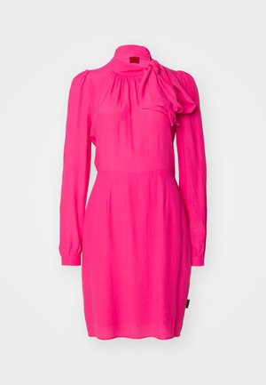 Haljina fuksija ružičaste boje s dugim rukavima, naboranim dekolteom i naglaskom u obliku mašne na ramenu. Izrađena je od laganog materijala.