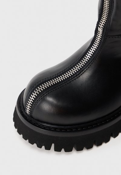 Botte en cuir noir avec semelle à épaisseurs et fermeture éclair centrale en métal argenté allant de l'orteil à la cheville.