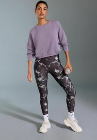 Lilla lühikas sweatshirthoodie, must marmormusterega retuus, valged tennised, hall veepudel käes. Siledad kangad, mugav lõige.