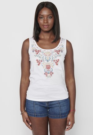 T-shirt sans manches blanc avec une broderie florale multicolore à l'avant, encolure ronde et emmanchures larges, associé à un short en denim.