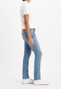 Ljusblå denimjeans med slim fit, utrustade med en läderlapp på midjan. Kombineras med en vit t-shirt med kort ärm och vita sneakers.