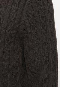 Dunkelbrauner gestrickter Pullover mit einem Kabelmuster und strukturierten vertikalen Linien. Der Stoff wirkt weich und dick und lässt auf Wärme schließen.