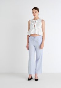 Top peplum bianco con dettagli annodati sul davanti abbinato a pantaloni a palazzo azzurri con motivo. Tacchi neri completano l'outfit. Design semplice e contemporaneo.