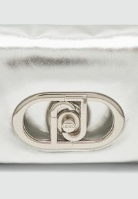 Srebrna metalna clutch torbica s glatkom teksturom, koja ima istaknut ovalni kopču s kružnim detaljem i ugraviranim logotipom marke.