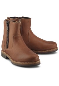 Botines de cuero marrón con cremalleras laterales, punteras redondas, costuras visibles y tacones bajos apilados sobre fondo blanco.