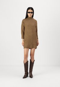Brun strikket kjole med høy krage, trekvart ermer og sideslits, paret med mørkebrune cowboystøvler med intrikate motiver.