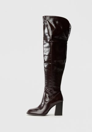 Bottes en cuir bordeaux glacé montant jusqu'au genou, avec un bout carré et un talon bloc, présentant un design ample et des détails de couture minimalistes.