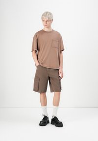 Brun bomulls T-skjorte med korte ermer og brystlomme, sammen med brune cargo-shorts med flere sidelommer og en avslappet passform.