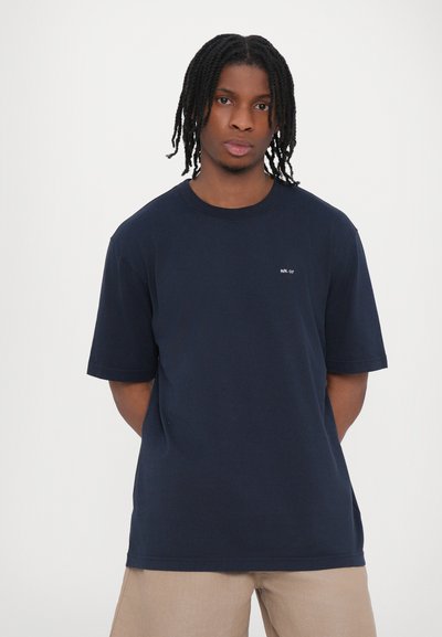 T-shirt en coton bleu marine à manches courtes, col rond, avec un petit logo blanc sur la poitrine. Conception simple et coupe décontractée.