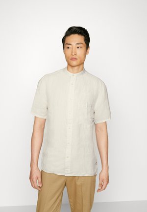 Camisa de lino beige de manga corta con cuello alzado, cierre frontal de botones, un bolsillo en el pecho y sutiles acentos de la marca.