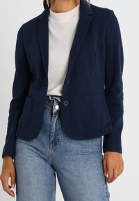 Marinblå blazer i mjukt tyg, med en knappknäppning, slagkrage och två framfickor. Matchas med högmidjade jeans.