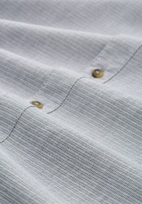 Tissu tissé gris clair avec un motif texturé; présente un détail de bouton jaune et un léger brillant.