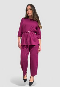 Outfit color prugna composto da una maglietta a maniche corte con vita cinturata e pantaloni larghi. Tacchi a punta neri completano il look.
