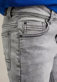 Sive traperice s izblijedjelim završetkom, s kontrastnim crnim šavovima, prednjim novčanikom i metalnim gumbima.
