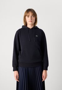 Sudadera azul marino en una mezcla de algodón, con un bolsillo canguro, capucha con cordones y un pequeño logotipo verde bordado en el pecho.