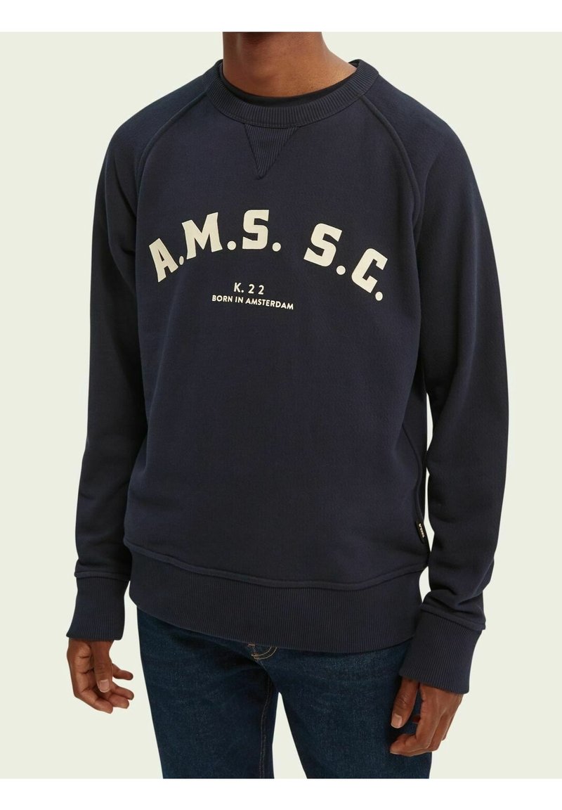 Sweat-shirt col rond marine en tissu doux avec poignets et ourlet côtelés. Présente un texte imprimé blanc : "A.M.S.S.C K.22 NÉ À AMSTERDAM."