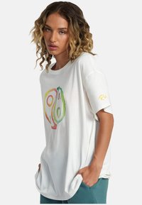 Camiseta blanca de manga corta con un diseño gráfico de aguacate colorido. Tela suave con un corte holgado y bolsillos laterales en la parte inferior.