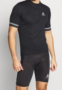Černé cyklistické triko s krátkým rukávem a čtvrtinovým zipem, s bílými pruhovanými akcenty na rukávech. Černé cyklistické šortky s polstrovanou vložkou.