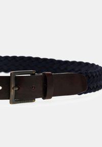 Geflochtener dunkelblauer Stoffgurt mit dunkelbraunem Lederband und antikisiertem Messingschnallen, die mit "GUESS" graviert ist.