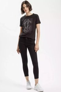 Czarna bawełniana koszulka z graficznym wzorem ozdobionym metalowymi ćwiekami, w połączeniu z czarnymi dżinsami i białymi trampkami. Gładka faktura, luźny krój.