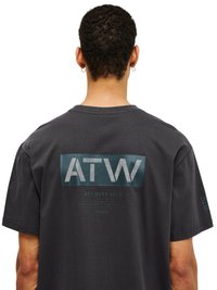 Person, die ein schwarzes T-Shirt mit der Aufschrift „ATW“ und „OFF DUTY GEAR“ auf dem Rücken trägt, von hinten vor weißem Hintergrund gesehen.