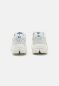 Baskets de sport blanches avec une finition texturée, présentant un talon surélevé, des accents de logo bleus et une semelle en caoutchouc à motif.