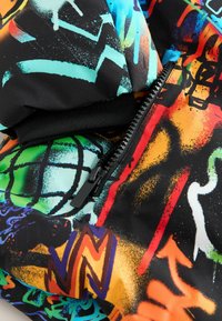 Gros plan sur un tissu coloré avec une fermeture éclair noire et des motifs de graffiti abstraits en vert, orange, rouge, bleu et noir.