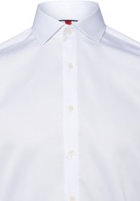 Camicia bianca con colletto a punta, dotata di chiusura frontale con bottoni bianchi e un tessuto morbido e strutturato.