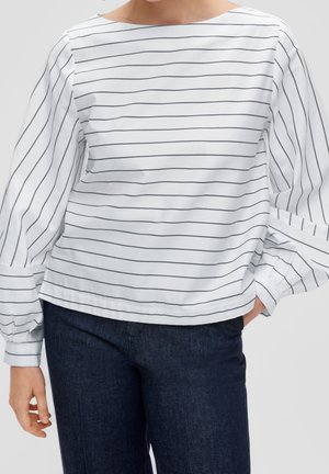 Witte blouse met dunne zwarte horizontale strepen en lange opgeblazen mouwen, gecombineerd met donkerblauwe spijkerbroek.