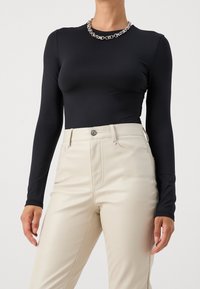 Långärmad svart åtsittande topp i kombination med höga beige fusk-läderbyxor. En kraftig silverkedja ger en kontrast.