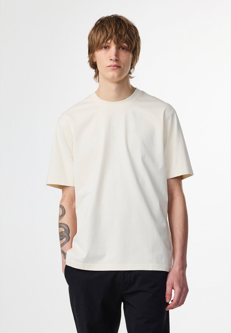 Simpel cremet bomulds t-shirt med korte ærmer, rund hals og en afslappet pasform. Ingen mønstre eller dekorationer synlige.