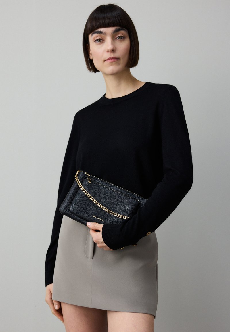 Fekete kötött pulóver hosszú ujjakkal; szürke miniszoknya; fekete bőr táska arany lánccal és cipzárral; sima textúra; egyszerű design.