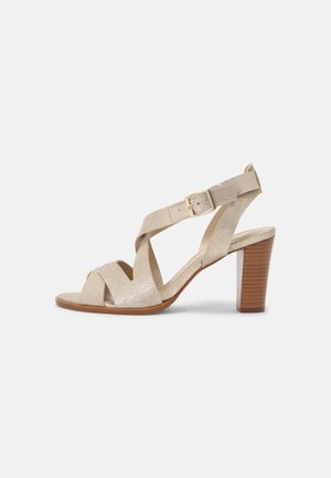 Sandale à lanières pailletée dorée avec talon carré, bout ouvert, et bride de cheville ajustable avec boucle dorée. Semelle intérieure et semelle en cuir lisse.