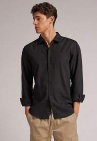 Zwarte button-up shirt van lichtgewicht stof met lange mouwen, opgerolde manchetten en een rechte zoom. Soepele textuur zonder patronen of accenten.