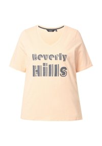 Světle broskvové tričko s véčkovým výstřihem a krátkými rukávy, které má grafický design s nápisem "Beverly Hills" v tlustých tmavě šedých písmenech.
