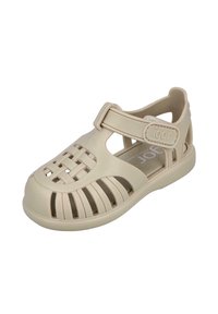 Sandalia de goma beige con diseño trenzado, lados abiertos, correa ajustable y suela texturizada para mayor agarre. Ligera y con puntera redondeada.