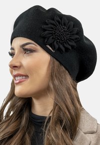Berretto a maglia nero con un accento floreale composto da petali di stoffa nera e un centro di perline. Texture liscia, forma rotonda e vestibilità aderente.